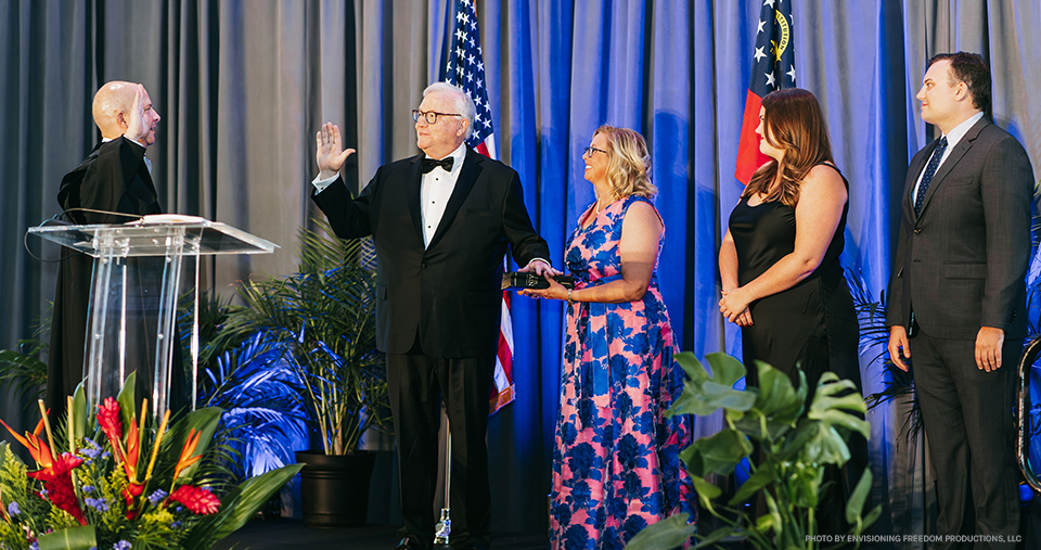 A judge is swearing-in a man wearing a tuxedo who is surrounded by his family.