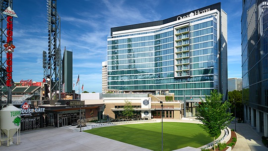 A large building stands prominently with a lush green lawn in front and the Chophouse Gate of Truist Park to the left.