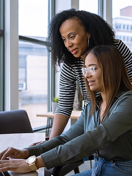 Two women collaborating on a laptop, focused on their work in a bright and modern office environment.