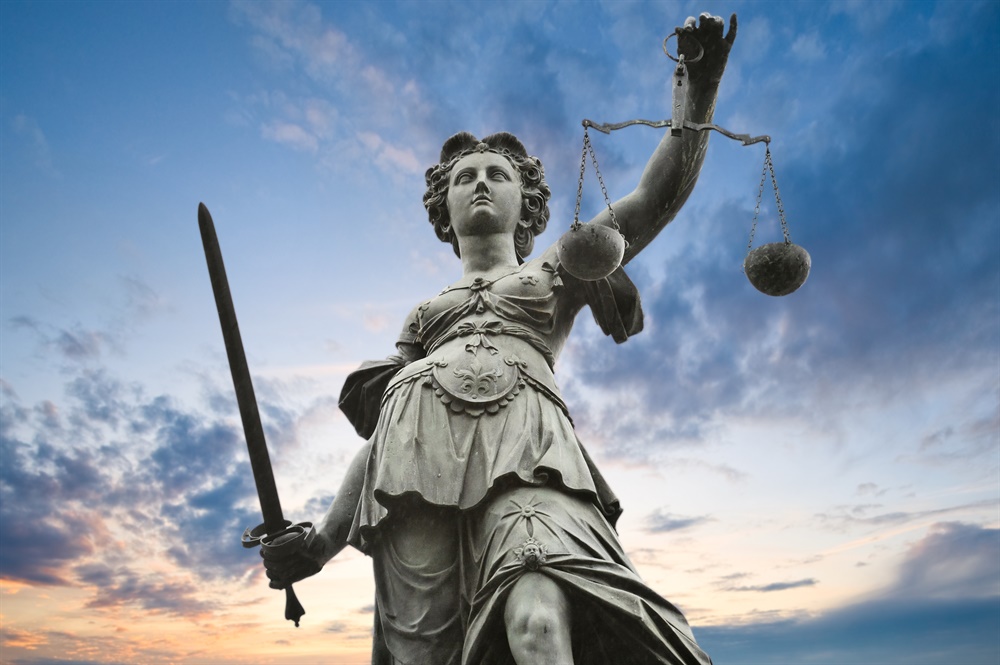 A statue of Lady Justice against a blue and orange sky.