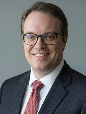 A smiling man wearing glasses and a suit with a red necktie.