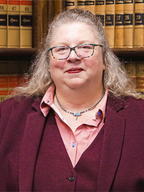 Woman with long blond hair and glasses in front of shelves of legal books.
