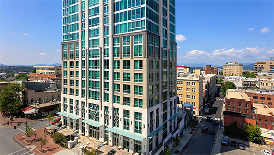 A stone and glass building stands tall against a blue sky in a city center.
