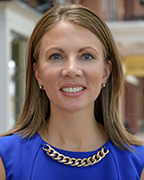 Woman wearing a royal blue dress embellished with a thick gold chain at the neckline.